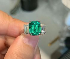 an emerald and diamond ring being held by someone