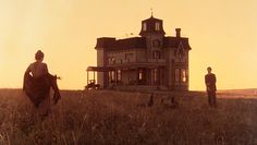 two people standing in front of a large house on a hill with birds flying around