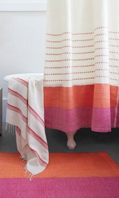 a bathroom with a pink rug and white bathtub next to the shower curtain that has an orange stripe on it