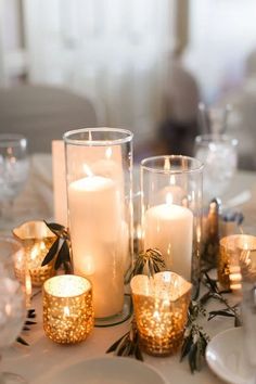 candles are lit on a table with white plates and silverware