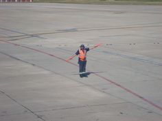 a man in an orange vest is standing on the tarmac with his arms outstretched