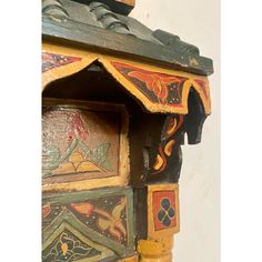 an old wooden clock with ornate designs on it's face and sides, painted in yellow, green, red and orange