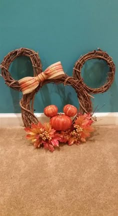 a mickey mouse wreath with pumpkins and fall leaves on the floor in front of a blue wall