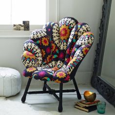 a colorful chair sitting in front of a mirror next to a white ottoman and rug