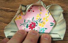 a hand holding a piece of fabric with flowers on it and a pink flowered origami hexagon