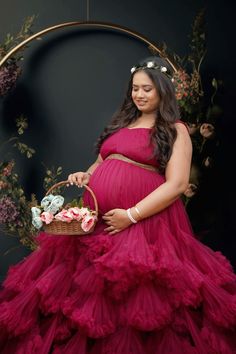 a pregnant woman in a red dress holding a basket with flowers on it and smiling