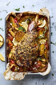 a roasting pan filled with chicken, potatoes and lemons on top of a table