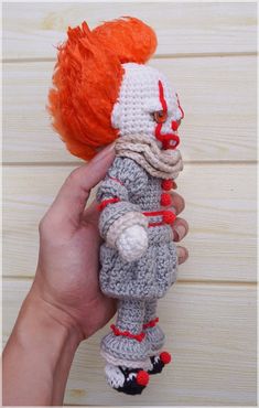 a hand holding a crocheted doll with an orange hair and red nose on it's head