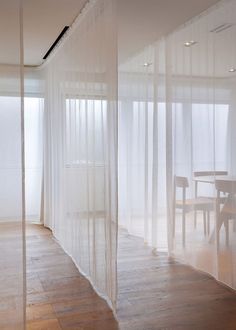 an empty room with sheer curtains on the walls and wooden flooring in front of a dining table