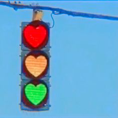 a traffic light with hearts painted on the red, green and yellow lights in front of a blue sky