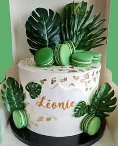 a white cake with green macaroons and palm leaves on top that says leonie