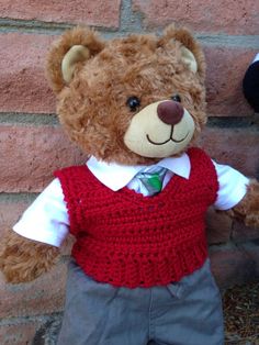 a teddy bear wearing a vest and tie standing next to a brick wall with his hands in his pockets