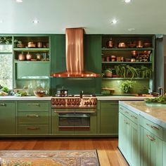 a kitchen with green cabinets and copper pots on the stove top, along with an area rug