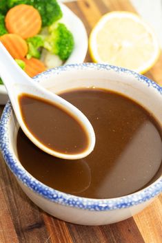 a bowl filled with brown liquid next to a plate of broccoli and carrots