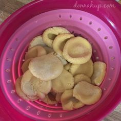 a pink colander filled with cut up cookies in it's drainer on a wooden table