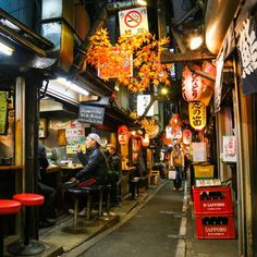 an alley way with people sitting at tables and signs hanging from the ceiling above them