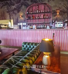 a green couch sitting in front of a bar with a lamp on it's side