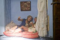 two women are sitting on a bed and one is holding a cup in her hand