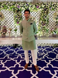 a man standing in front of a table with flowers and greenery on it's wall