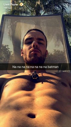 a man with no shirt on laying down in front of a palm tree and looking at the camera