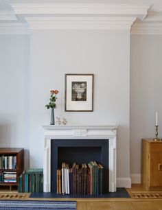 a living room with a fireplace, bookshelf and pictures on the wall above it