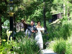 a bride and groom walking down a path in the woods with tall grass on either side