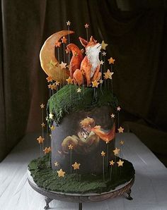 a cake decorated with moss and stars on a white table cloth covered tablecloth, featuring an image of a fox and the moon