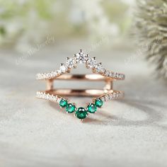 a diamond and emerald ring set on top of a white table next to a pine tree