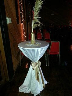 a white table topped with a wine bottle and a vase filled with flowers sitting on top of a wooden floor