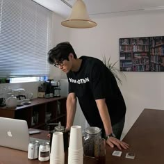 a man standing at a table with several cups on it and an apple laptop in front of him