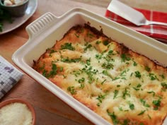 a casserole dish with cheese and herbs in it sitting on a wooden table