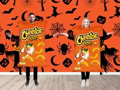 two people standing in front of a halloween themed wallpaper holding bags of cheetos