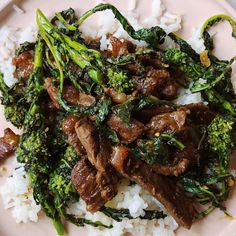 a pink plate topped with beef and broccoli covered in sauce on top of white rice