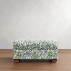 an upholstered footstool on a wooden floor in front of a white wall