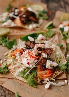 two tacos with meat, lettuce and cheese on top sitting on a piece of paper