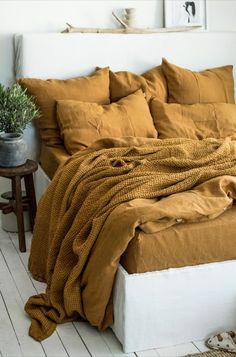 an unmade bed with brown sheets and pillows on it in a white room next to a potted plant