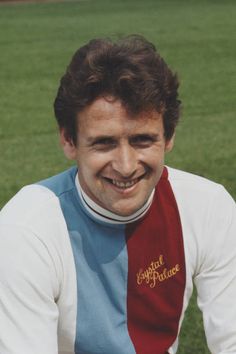 a man wearing a red, white and blue neck tie smiles at the camera while sitting on a soccer field