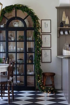 a dining room table and chairs covered in christmas greenery next to a china cabinet