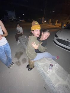 two people sitting on a bench in the middle of a parking lot at night with their arms around each other