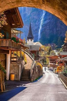 an arch leading into a village with mountains in the background and flowers growing on the side