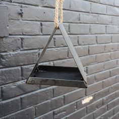 a metal bird feeder hanging from a rope on a brick wall with no one in it