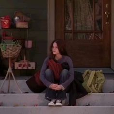 a woman sitting on the steps in front of a house with her hands folded up