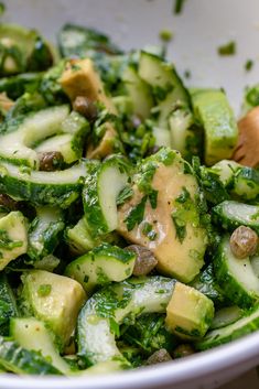 a white bowl filled with cucumbers and other veggies next to a wooden spoon