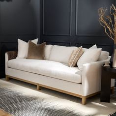 a white couch sitting in front of a black wall next to a table with a vase on it