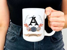 a woman is holding a coffee mug with the letter a in front of her back