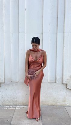 a woman standing in front of a white wall wearing a pink dress and holding a purse