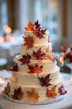 a wedding cake decorated with fall leaves on a table in front of candles and flowers