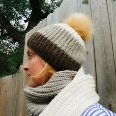 a woman wearing a hat and scarf next to a fence