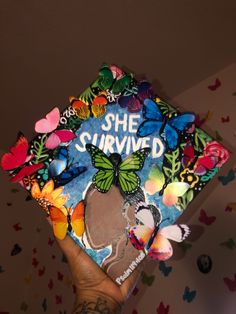 a person holding up a book with butterflies on it and the words she survived written on it