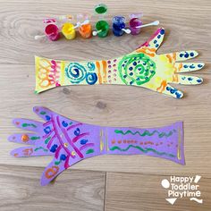 two handprinted paper gloves sitting on top of a wooden floor next to paint tubes